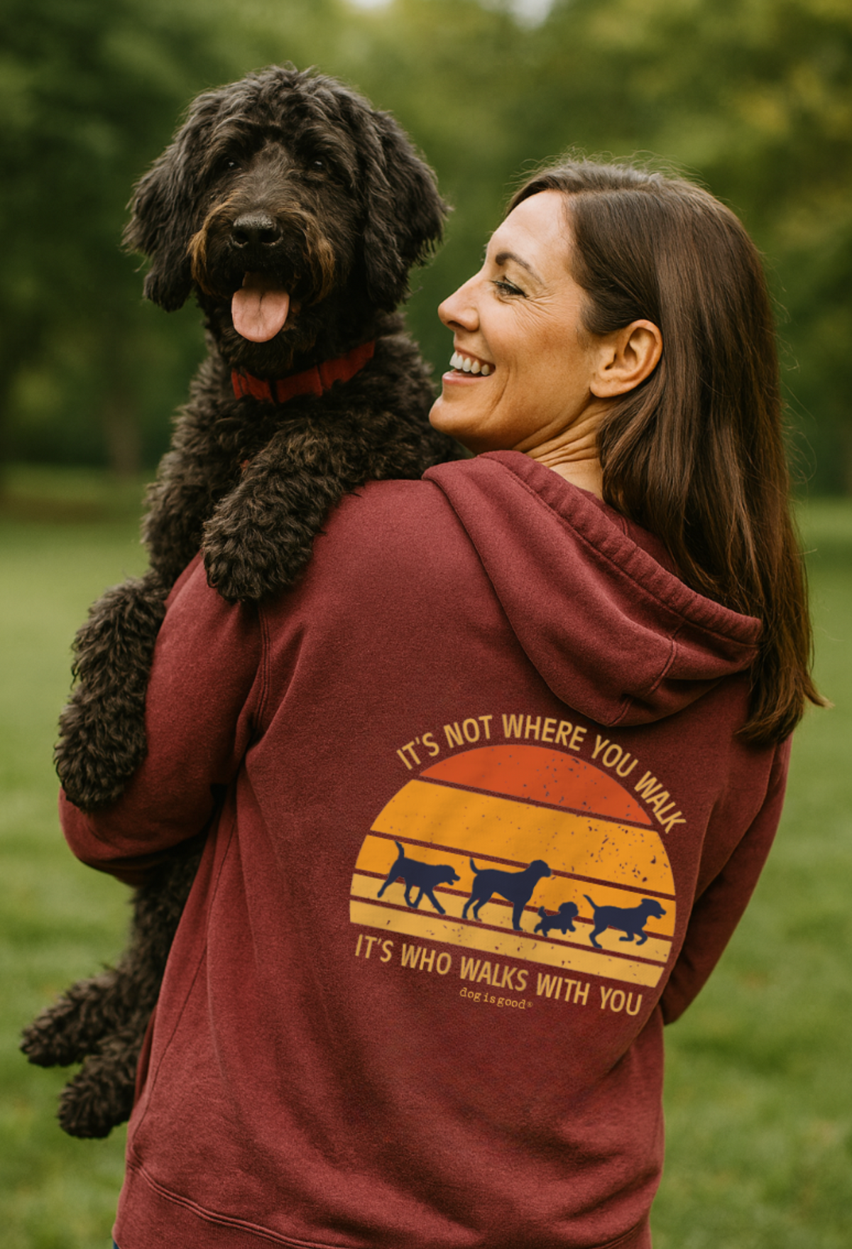 Woman smiles while holding a black dog, wearing a hoodie with a positive dog-related message.