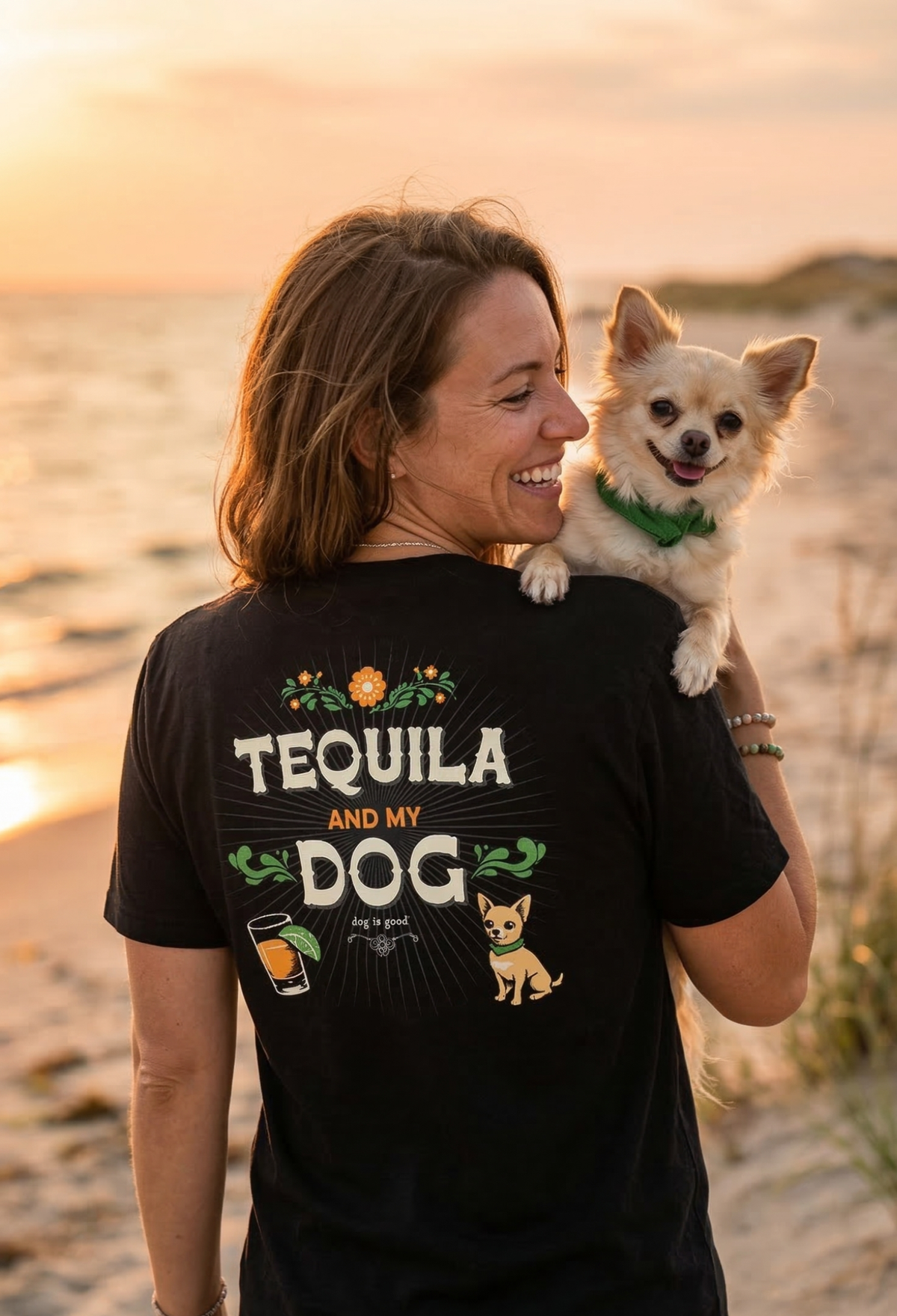 Woman wearing a black t-shirt with 'Tequila and My Dog' text and a dog on her shoulders at sunset.
